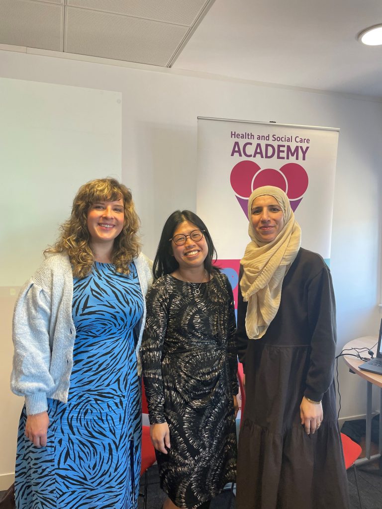 Photograph of Maxine Meighan, Jen Ang and Bushra Riaz standing in front of banner for the Health and Social Care Academy.
